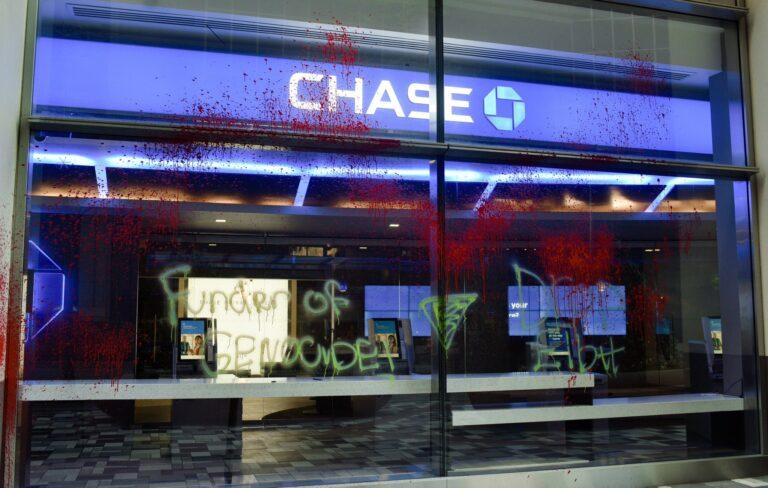 Chase Bank windows splattered with red paint. Graffiti reads "Funder of Genocide".