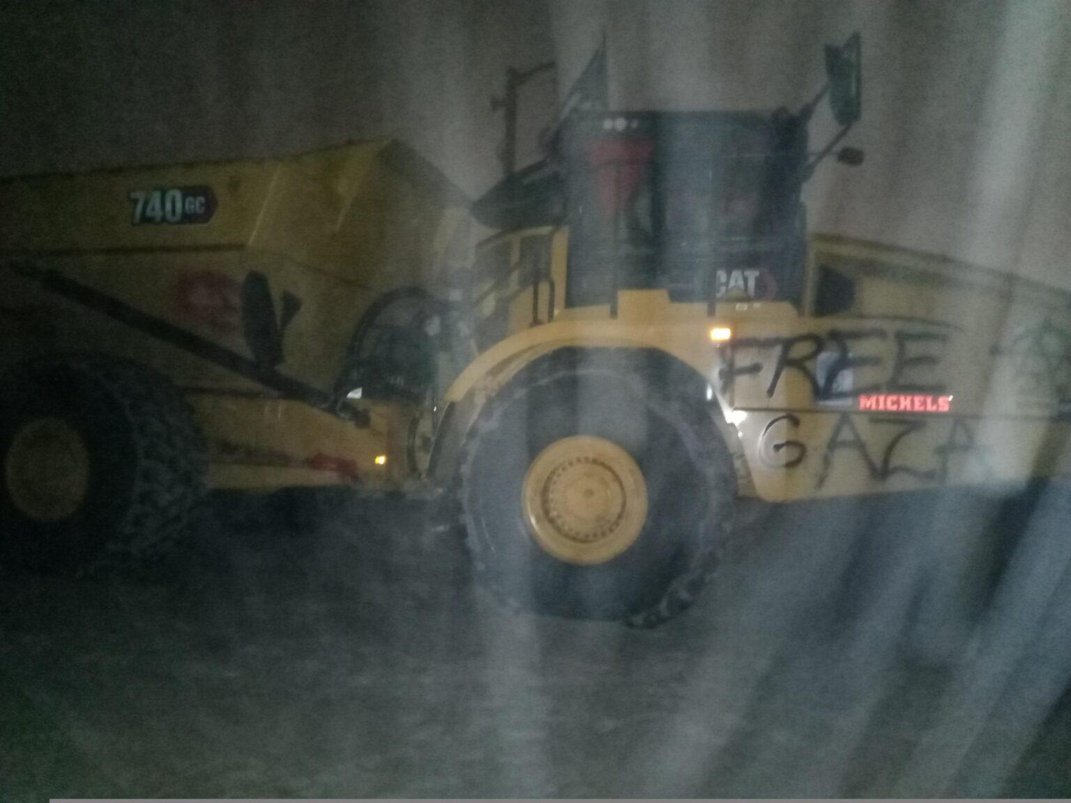 A vandalized CAT 740GC haul truck. Graffiti reads "FREE GAZA" with a circle-A and a red downward triangle.