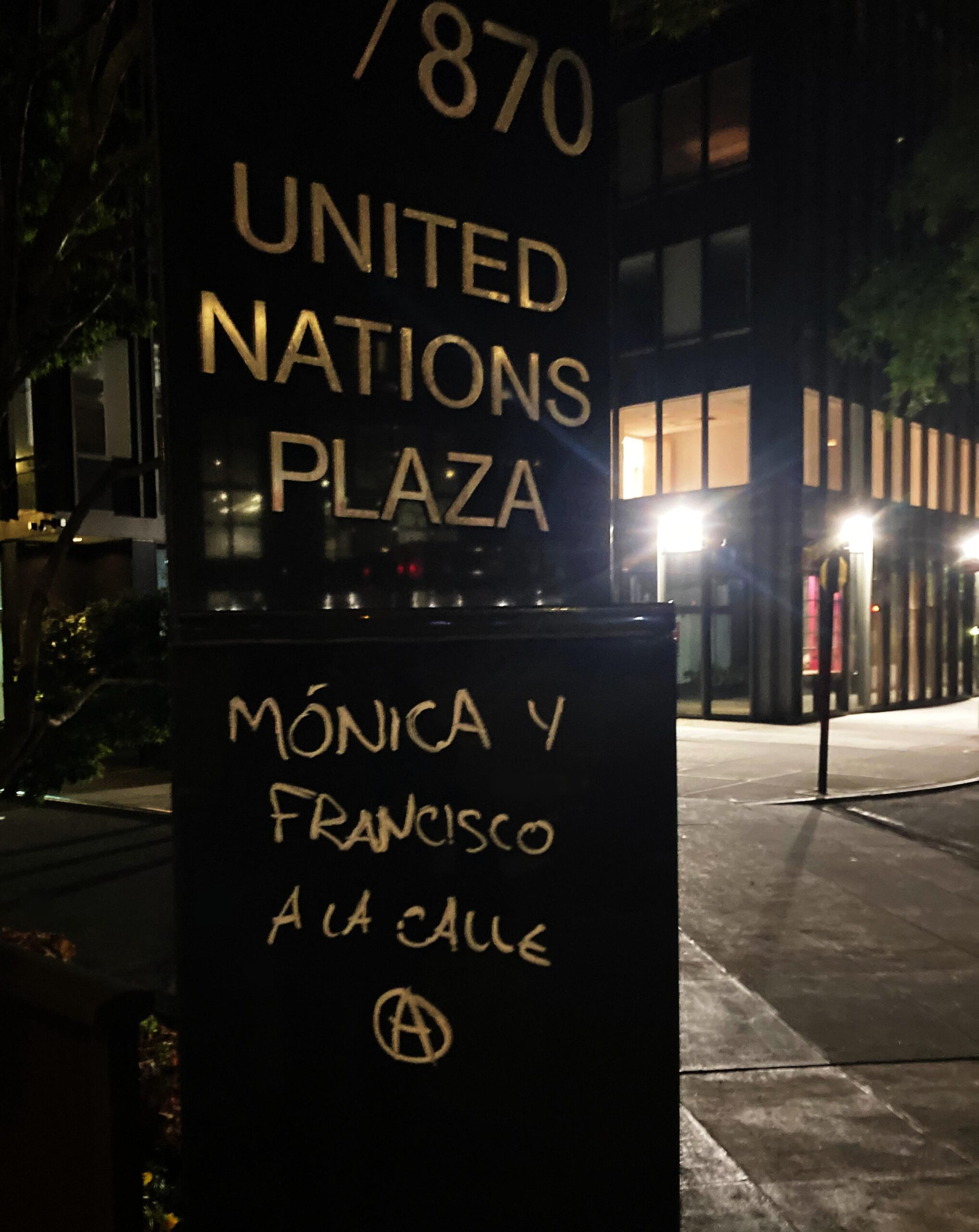 Sign reading "UNITED NATIONS PLAZA" with graffiti reading "Monica y Francisco a la calle" with a circle-A.